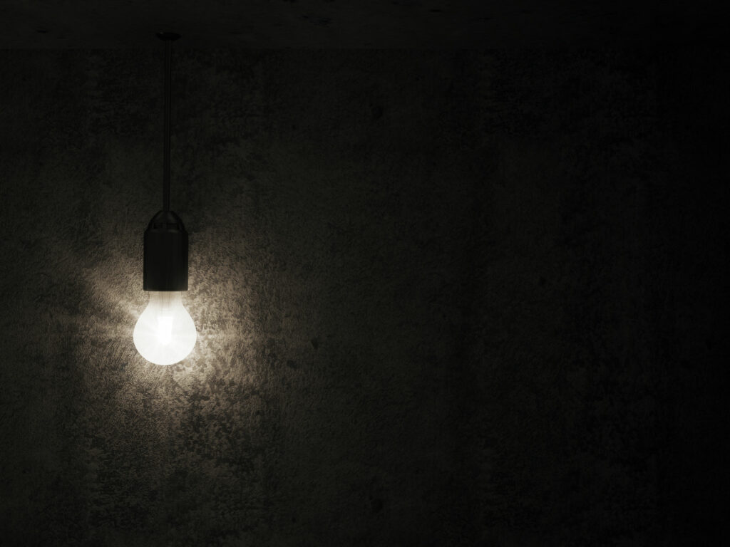 Lampada acesa, emanando luz branca, em um ambiente completamente apagado e preto.