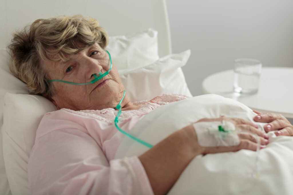 Mulher branca, idosa, deitada em cama de hospital.