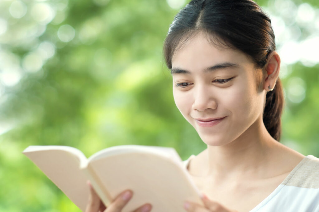 Mulher asiática lendo um livro, em pé em um parque