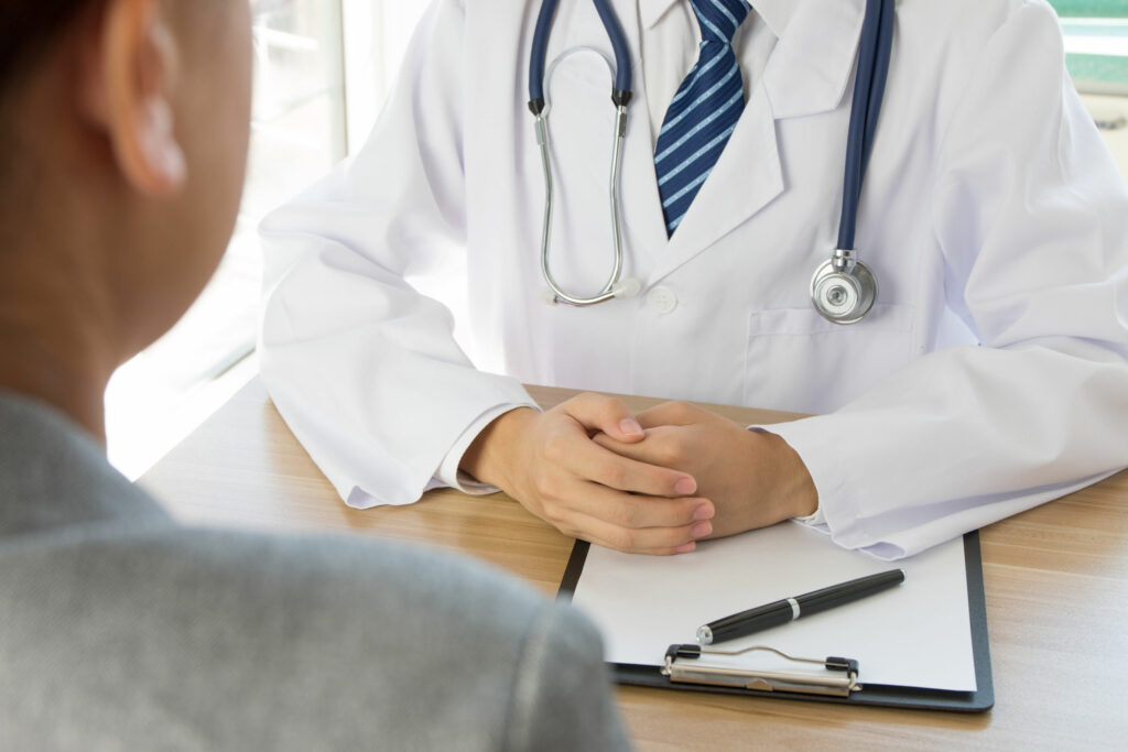 Médico sentado na mesa de consultório, atendendo um paciente.