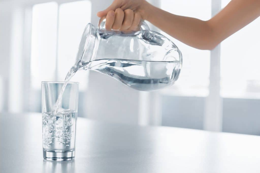 mulher colocando água de uma jarra em um copo.