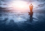 Silhueta de mulher praticando Yoga na praia de frente para o pôr do sol