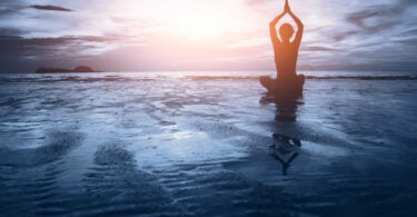 Silhueta de mulher praticando Yoga na praia de frente para o pôr do sol