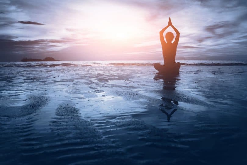 Silhueta de mulher praticando Yoga na praia de frente para o pôr do sol