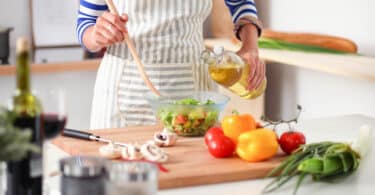 Mulher temperando salada de vegetais na cozinha.