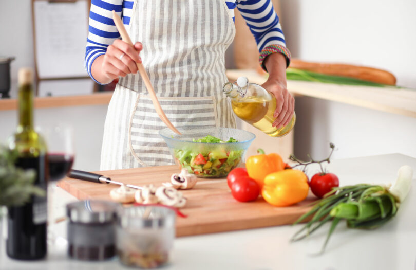 Mulher temperando salada de vegetais na cozinha.