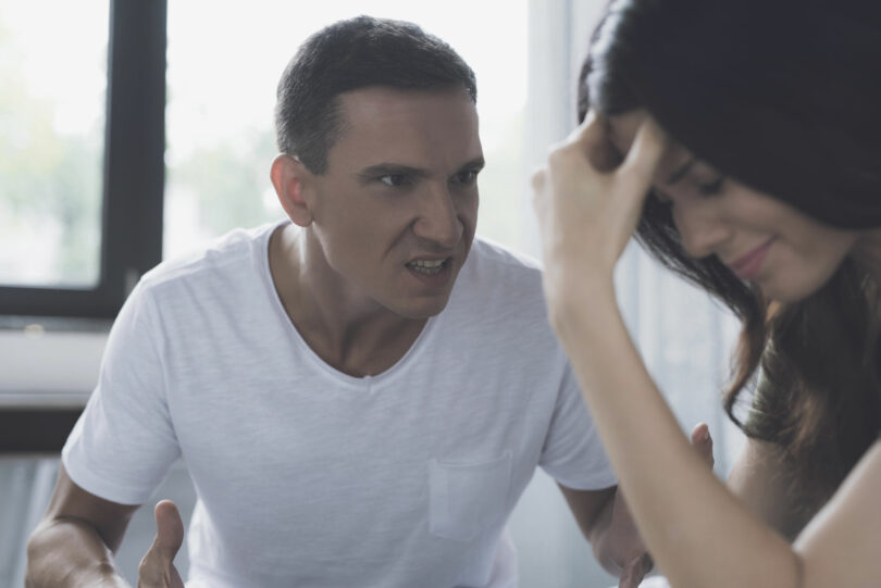 Homem e mulher discutindo. Mulher chorando, apoiando a cabeça em uma das mãos, enquanto o homem a observa com uma expressão de nervoso, como se estivesse gritando.