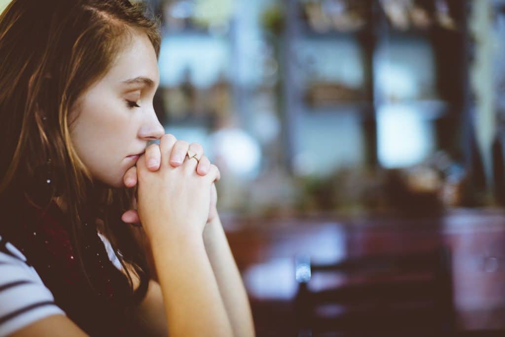 Mulher sentada em banco de igreja, com os olhos fechados, orando.