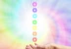 mão abaixo de uma fileira de círculos redondos iluminados cada qual com a cor de um chakra
