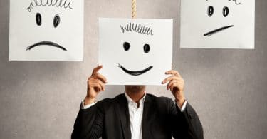Homem escondendo o rosto em uma placa com um rosto feliz no meio de duas outras placas com rostos tristes e chateados.