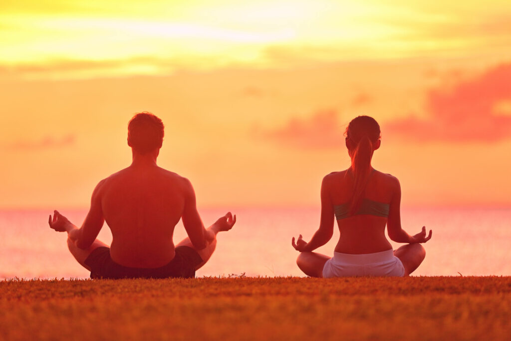 um casal sentado, meditando, de frente para o mar.