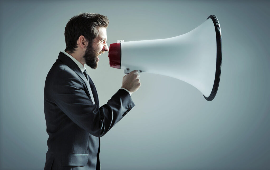 Homem vestido de social, gritando em uma megafone gigante