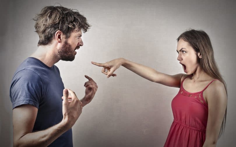 Homem e mulher discutindo. A mulher aponta o dedo para a cara do homem, enquanto este levanta os braços em sinal de irritação.