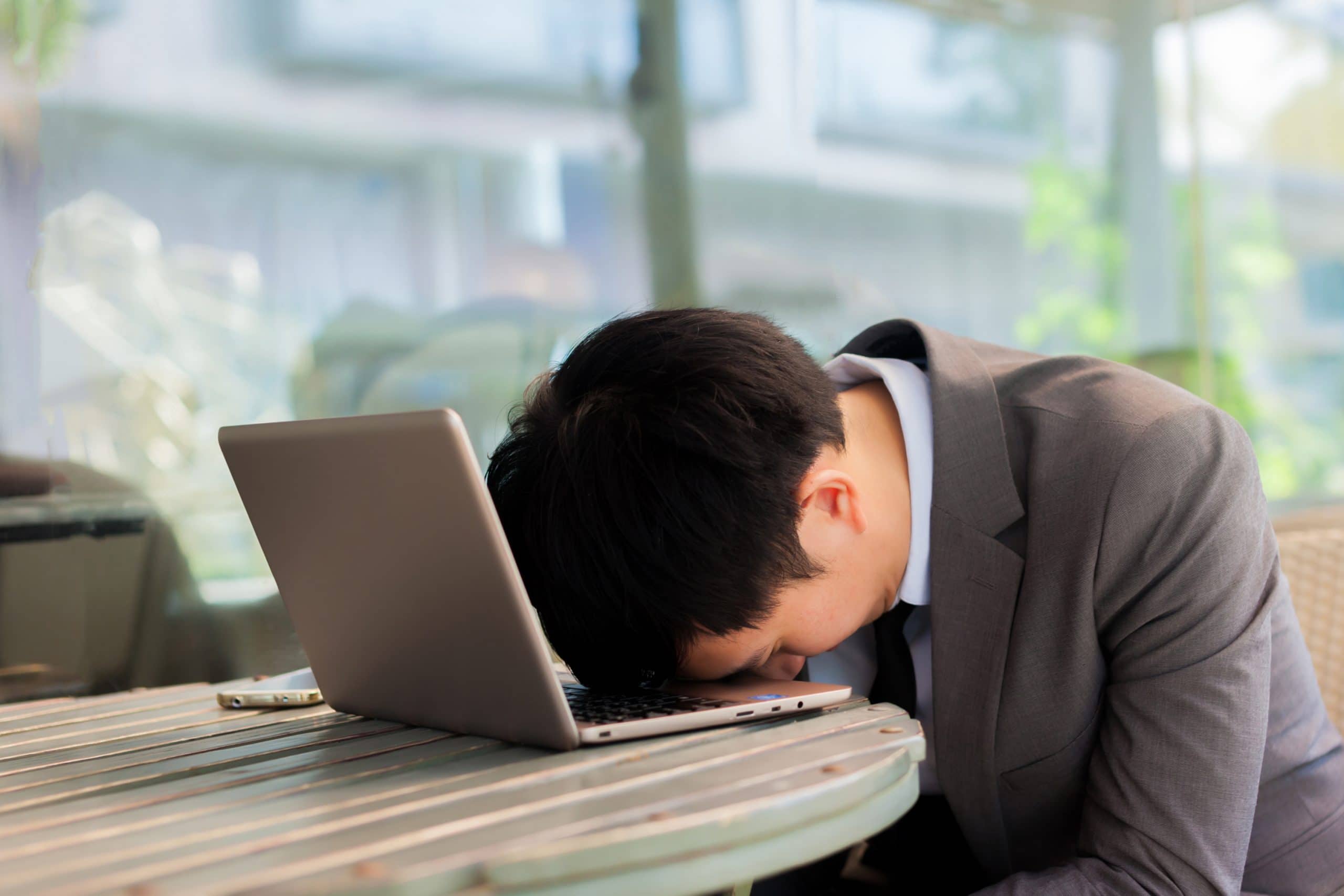 Homem cansado com a testa apoiada em seu laptop