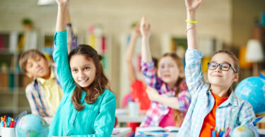 Crianças na sala de aula levantando a mão com sorriso no rosto