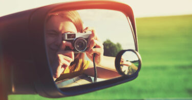 Meninha com máquina fotográfica vista pelo retrovisor de um carro