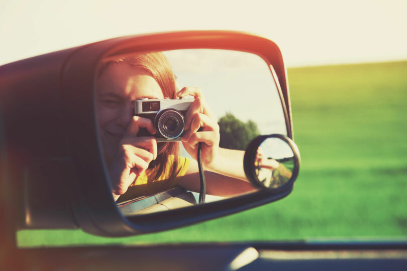 Meninha com máquina fotográfica vista pelo retrovisor de um carro