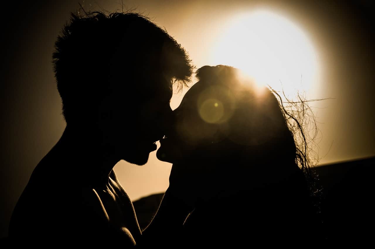 Silhueta de casal se beijando com sol refletindo no fundo