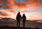 Casal de costas de mãos dadas com por-do-sol de fundo