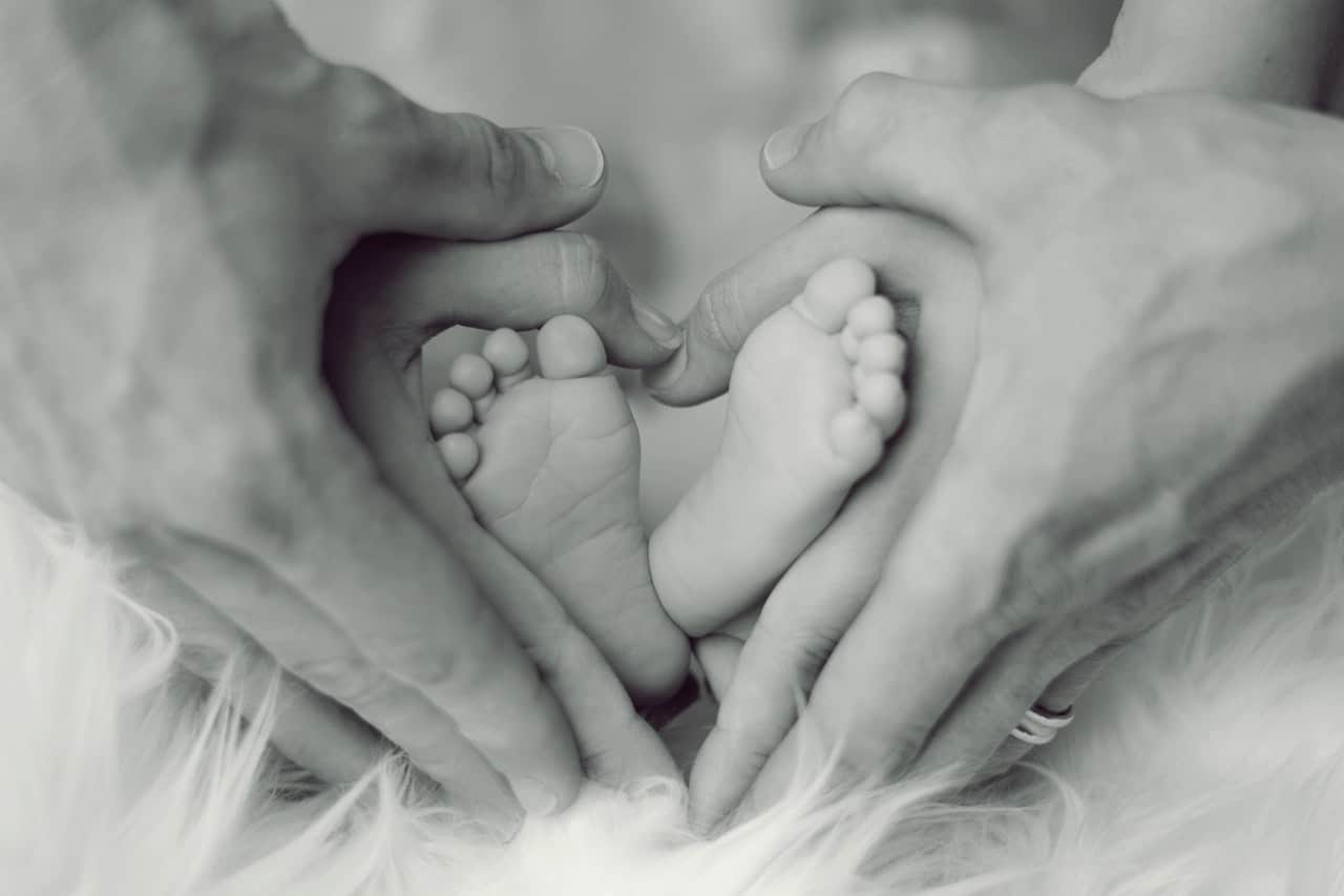 Mãos de pai e mãe fazendo coração em volta dos pés de um bebê