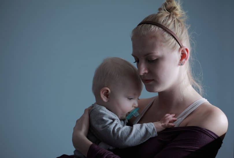 Mãe com olhar triste com filho bebê no colo