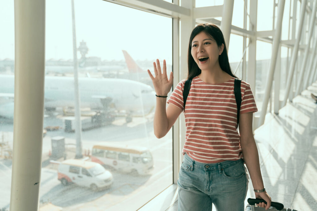 Mulher asiática, jovem, sorridente, cumprimentando alguém em um aeroporto