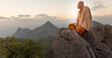 Monje budista meditando sobre montanhas.