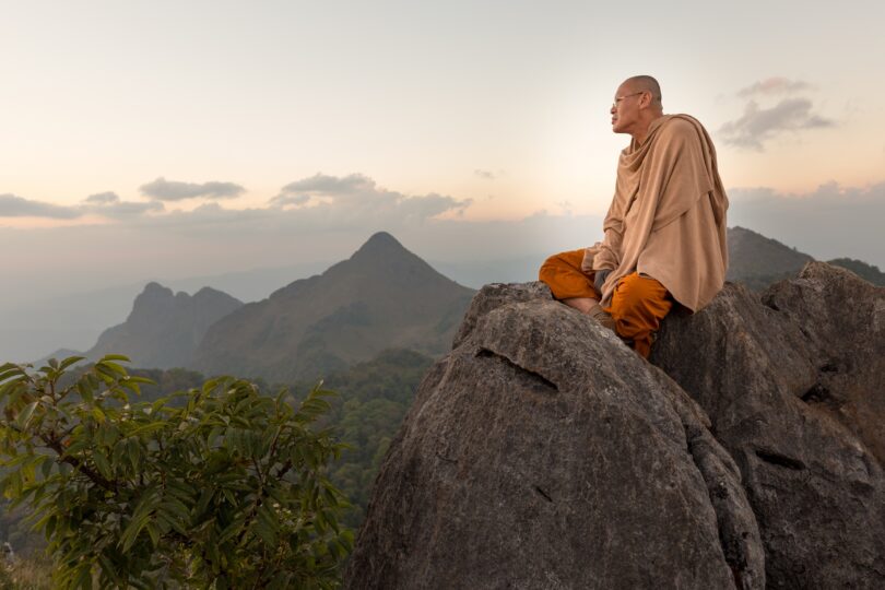 Monje budista meditando sobre montanhas.