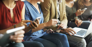Pessoas sentadas usando celular e computador felizes
