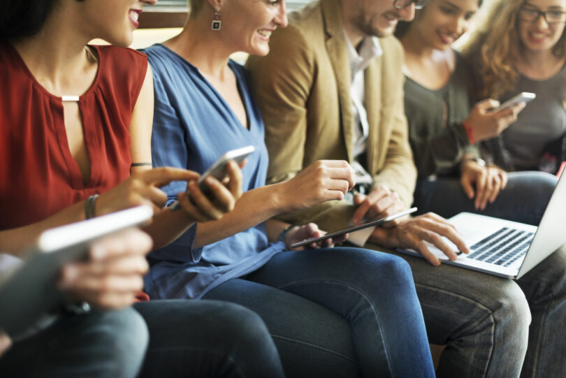 Pessoas sentadas usando celular e computador felizes