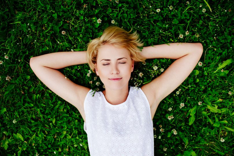 Foto de uma mulher deitada na grama sorrindo.