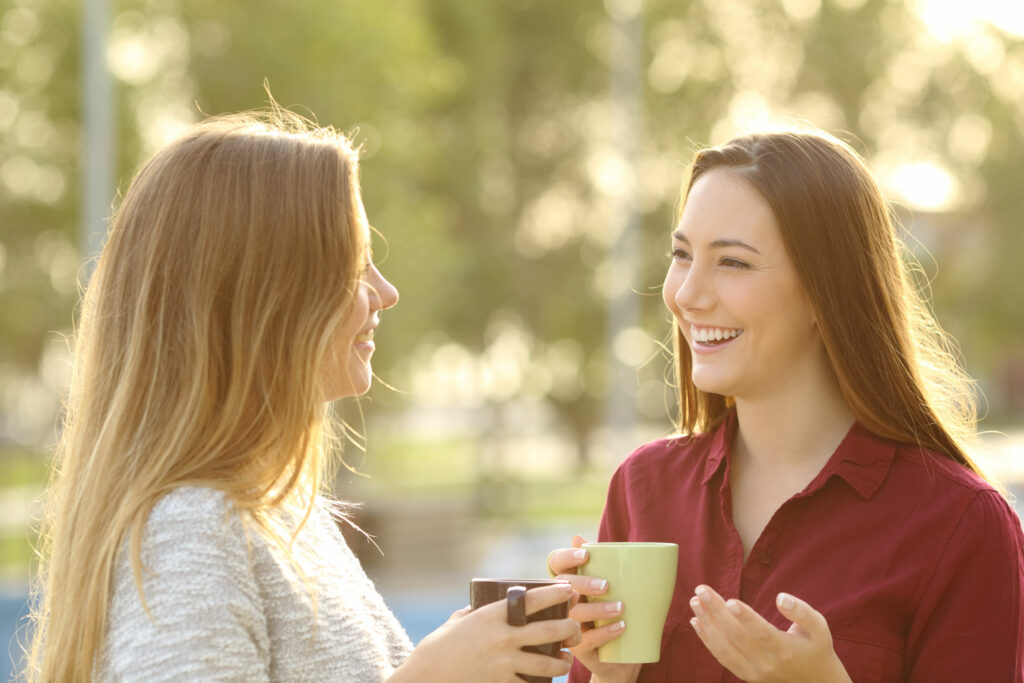 Duas mulheres jovens, sorridentes, tomando café em xícaras, conversando