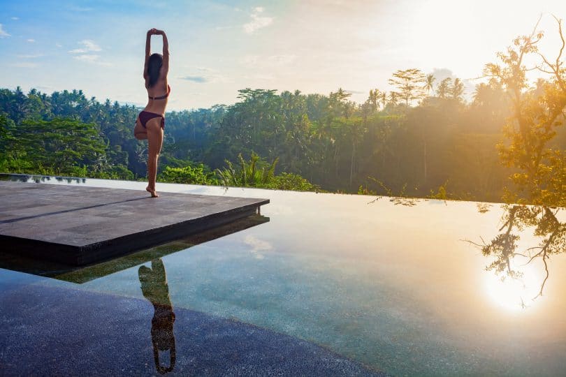 Retiro - Criatividade para reinventar sua vida Mulher fazendo yoga em cima de um pier de madeira em um lado, observando o nascer do sol.