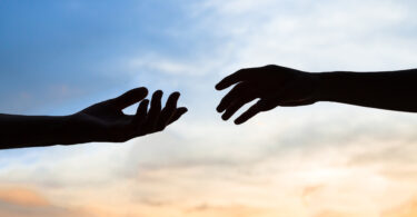 Duas mãos quase se tocando em frente ao céu.