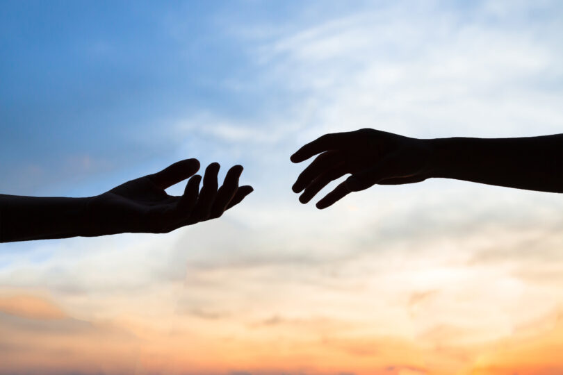 Duas mãos quase se tocando em frente ao céu.