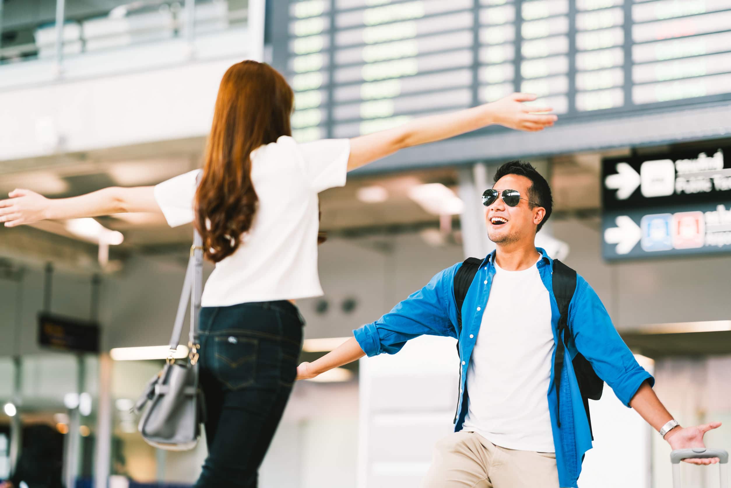 Homem e mulher, ambos asiáticos, felizes, correndo um em direção ao outro, se reencontrando em um aeroporto.