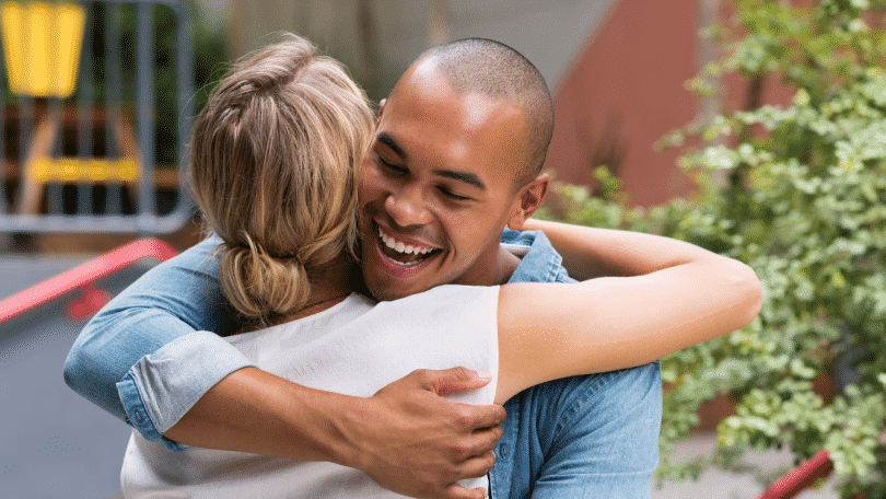 Um homem sorrindo e abraçando uma mulher