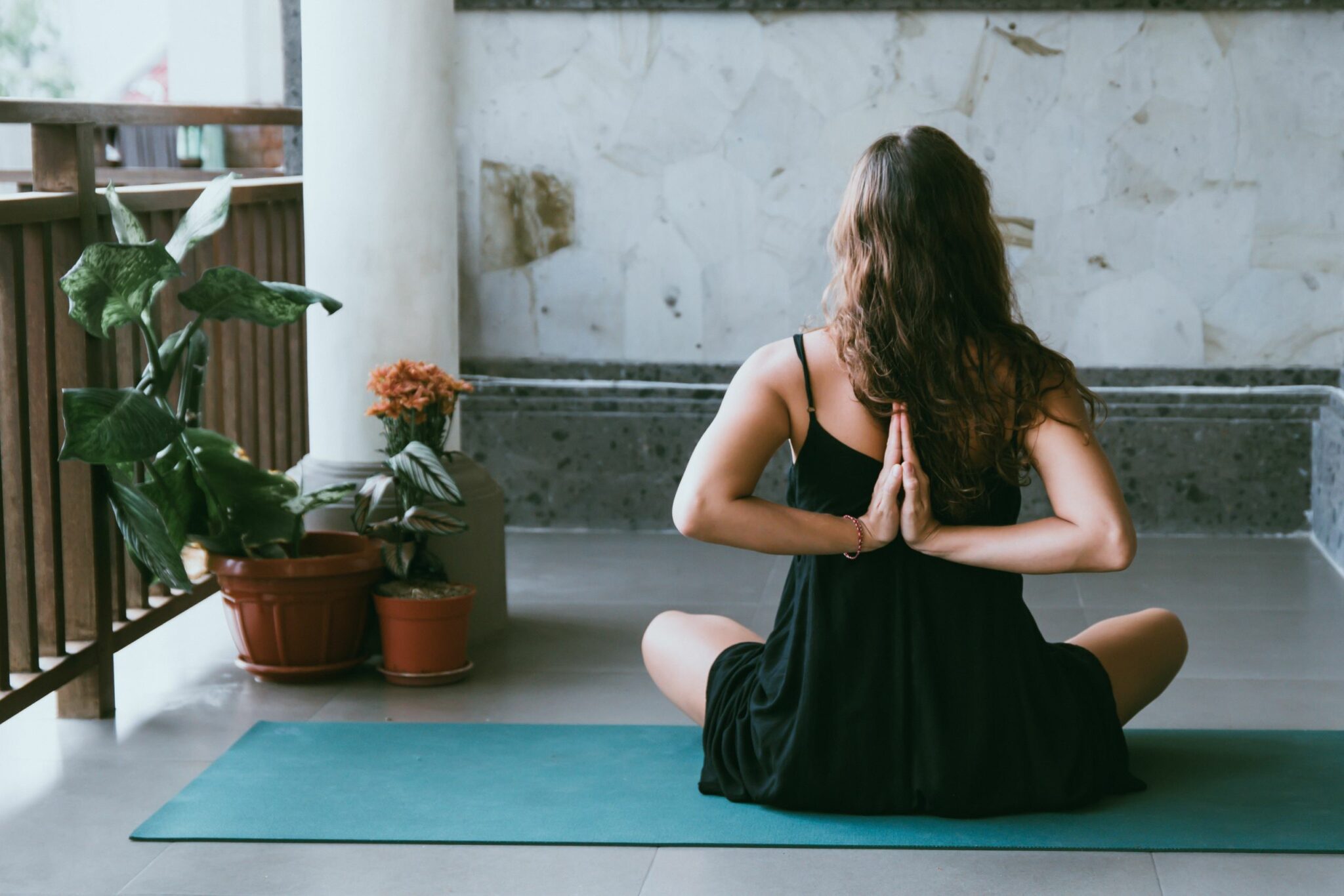 Mulher de costas em posição de meditação com braços nas costas sentada em tapete e plantas