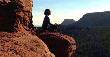 Mulher sentada sobre uma rocha em posição de meditação representando o eu sem fronteiras.