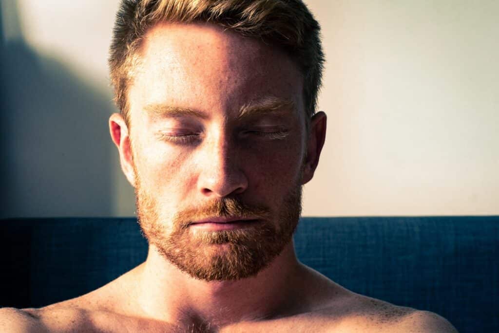 Homem sentado em um sofá, com os olhos fechados, meditando