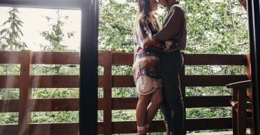 Casal relaxando na varanda, abraçando-se em uma cabana de madeira na floresta.