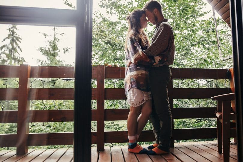 Casal relaxando na varanda, abraçando-se em uma cabana de madeira na floresta.