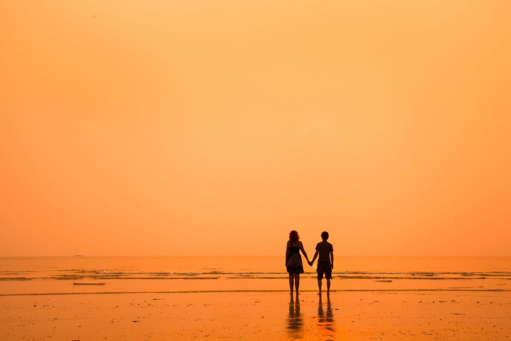 silhueta de duas pessoas caminhando na praia, de mãos dadas, no pôr do sol