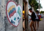 Muro com coração pintado com as bandeiras de Venezuela e Brasil pintadas escrito: Bem-vindos! E portão com pessoas entrando
