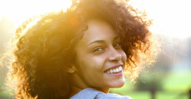 Mulher olhando de lado sorrindo com luz do sol ao fundo