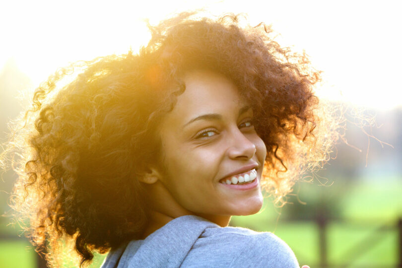 Mulher olhando de lado sorrindo com luz do sol ao fundo