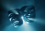 Duas máscaras de teatro com feições opostas sobre uma luz azul.