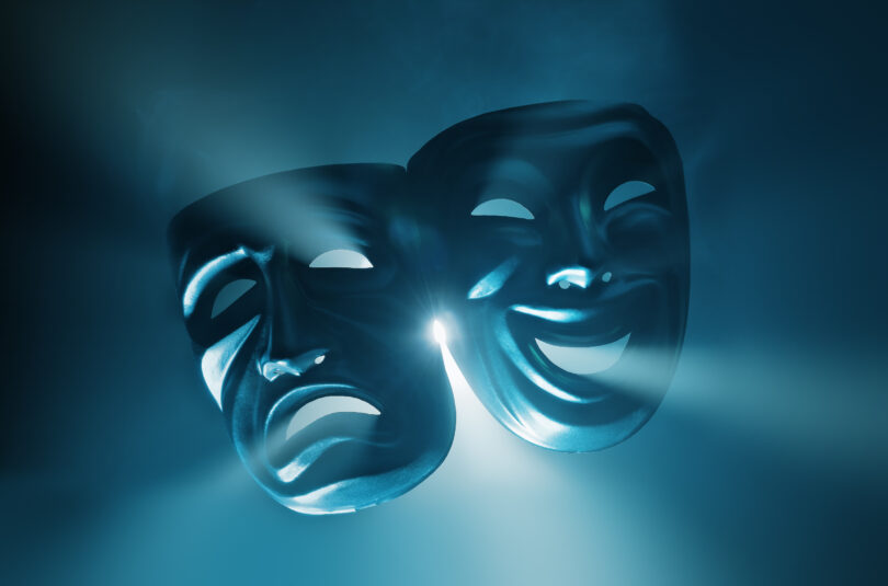 Duas máscaras de teatro com feições opostas sobre uma luz azul.