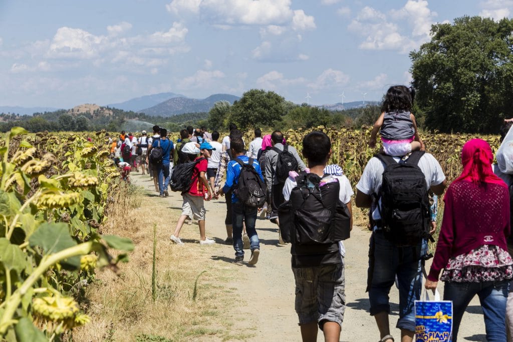 Grupo de pessoas, refugiados, caminhando em meio a uma plantação