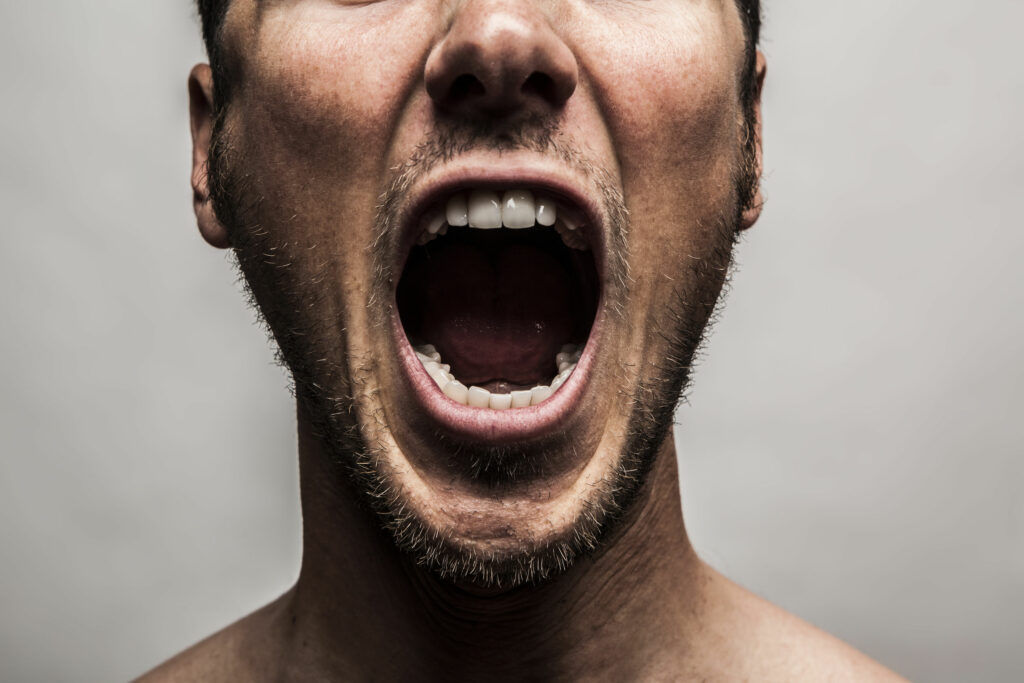 foto close do rosto de um homem branco, jovem, gritando de raiva